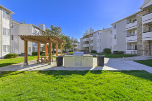 Exterior picnic area, lush grounds, pergola, picnic tables, outdoor grill area, residential buildings in the background, photo taken on a sunny day