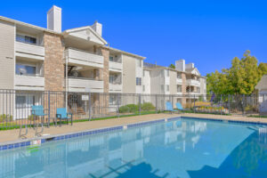 Exterior pool area, pergola in pool area, residential building in background, photo taken on a sunny day.