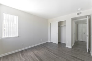Interior Unit Bedroom, neutral toned walls, wood floors, window adjacent to bedroom door, sliding closet door.