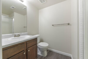Interior unit bathroom, wood floors, linoleum countertop, large vanity mirror, dark brown cabinetry.
